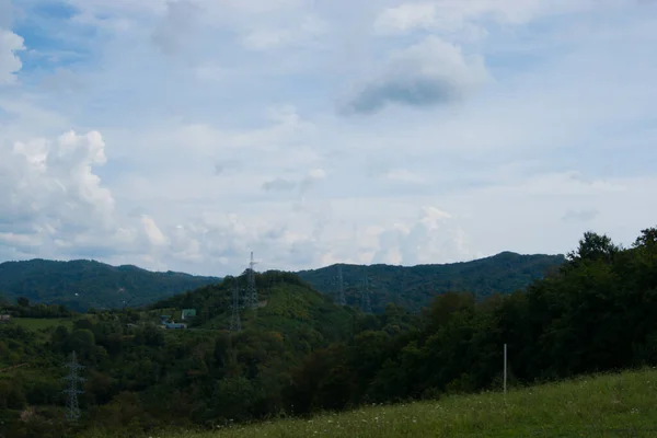 Noon in the mountains of the Caucasus - horizontal photo - mountain landscape. Blue sky with white clouds and beautiful mountain ranges completely covered with green trees.