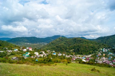 Yatay fotoğraf - Yaz dağı manzarası. Dağ köyleri, beyaz bulutlarda yeşil ve mavi gökyüzüne karşı renkli çatıları olan konutlar..