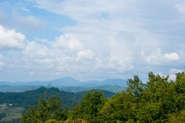 Noon in the mountains of the Caucasus - horizontal photo - mountain landscape. Blue sky with white clouds and beautiful mountain ranges completely covered with green trees.