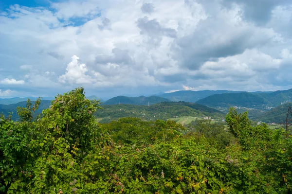 Noon in the mountains of the Caucasus - horizontal photo - mountain landscape. Blue sky with white clouds and beautiful mountain ranges completely covered with green trees.