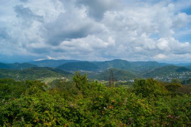 Kafkasya 'nın dağlarında öğle vakti - yatay fotoğraf - dağ manzarası. Beyaz bulutlu mavi gökyüzü ve yeşil ağaçlarla kaplı güzel sıradağlar..