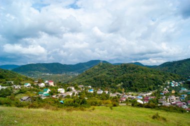 Yatay fotoğraf - Yaz dağı manzarası. Dağ köyleri, beyaz bulutlarda yeşil ve mavi gökyüzüne karşı renkli çatıları olan konutlar..
