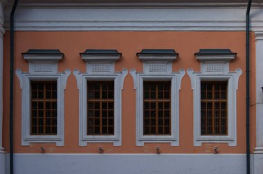 Eski bir binanın turuncu duvarında parmaklık olan beyaz çerçeveli pencereler. Eski model. Antik mimari. Hikaye. Tasarım