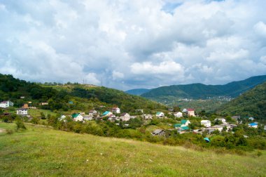 Yatay fotoğraf - Yaz dağı manzarası. Dağ köyleri, beyaz bulutlarda yeşil ve mavi gökyüzüne karşı renkli çatıları olan konutlar..