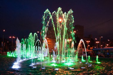 Bahçe düzenleme - koyu mavi bir gece gökyüzüne karşı parlak yeşil ışıklarla aydınlatılmış güzel bir çeşme. Aydınlatma, gece, ışıklar, parlaklık, peri masalı, gerçeküstü, güzellik
