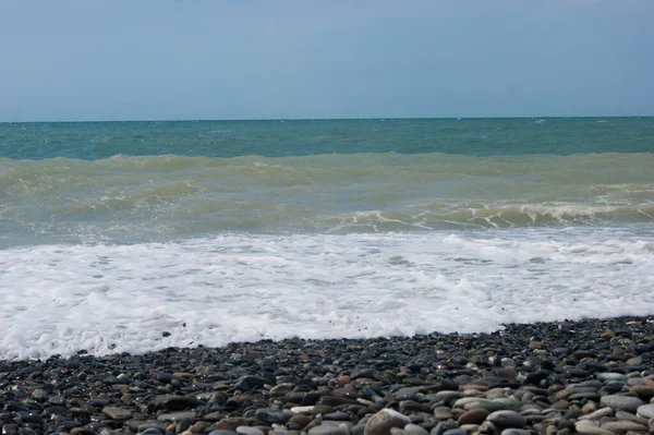 Morze niepokoi się raz - trochę błotnistej wody Morza Czarnego po małej burzy. Morze, czyste niebo i gładka linia horyzontu, fala, mokre duże kamyki na plaży. — Zdjęcie stockowe