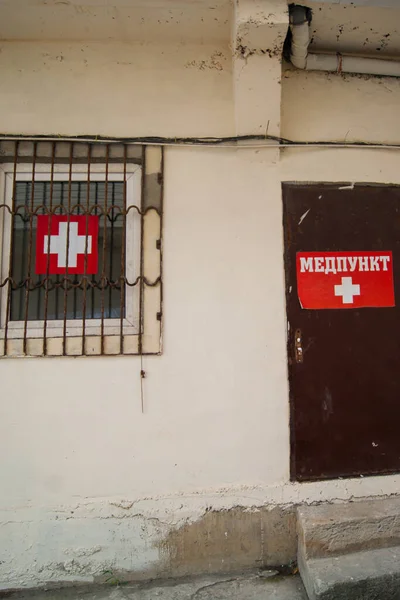 The center of medical care - the inscription on the sign, the translation from the Russian - the medical center. The building, decorated with light plaster, a metal brown door with two steps, a window with a lattice. Caucasian Mountains Summer