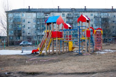 Şehir merkezinin avlusundaki çocuk parkında beş katlı bir evin arka planına karşı. Bölgeden yasaklayıcı kurdeleler koparılmış..