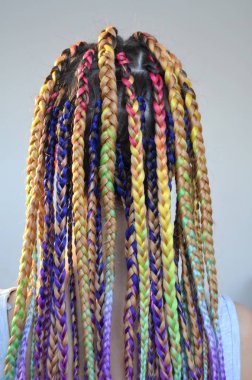 A girl with a fashionable set of multicolored braids Kanekalon. Colored artificial strands of hair. Material for plaiting braids. clipart