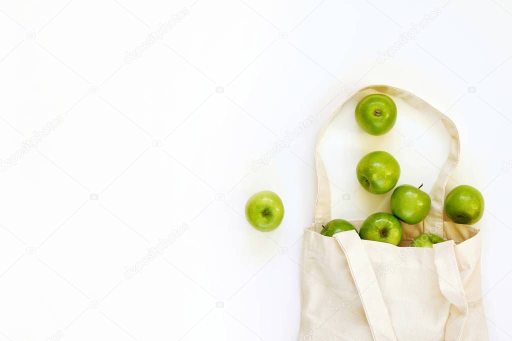 Reusable cotton textile bag with green apples on a white background. The concept of zero waste, green shopping. Top view with copy space for text.