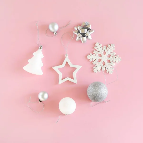 Pastel pembe arka planda beyaz ve gümüş süslemelerin Noel kompozisyonu. Minimalist tatil konsepti. Kare, üst manzara, düz uzanma.