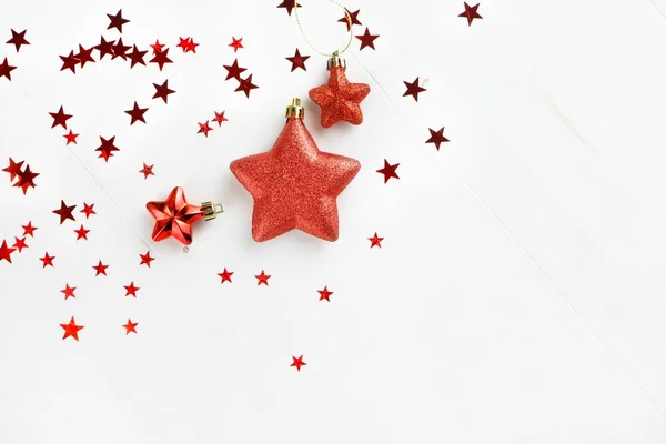 Kırmızı yıldızların dekorasyonları ve beyaz arka planda konfeti gibi düz bir Noel arkaplanı vardı. Minimalist tatil konsepti. Kopyalama alanı olan üst görünüm.