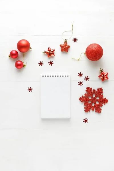 Christmas composition of a notebook made of red Christmas decorations and confetti. New Year\'s concept of planning, congratulations and wishes. Top view, flat lay with copy space.