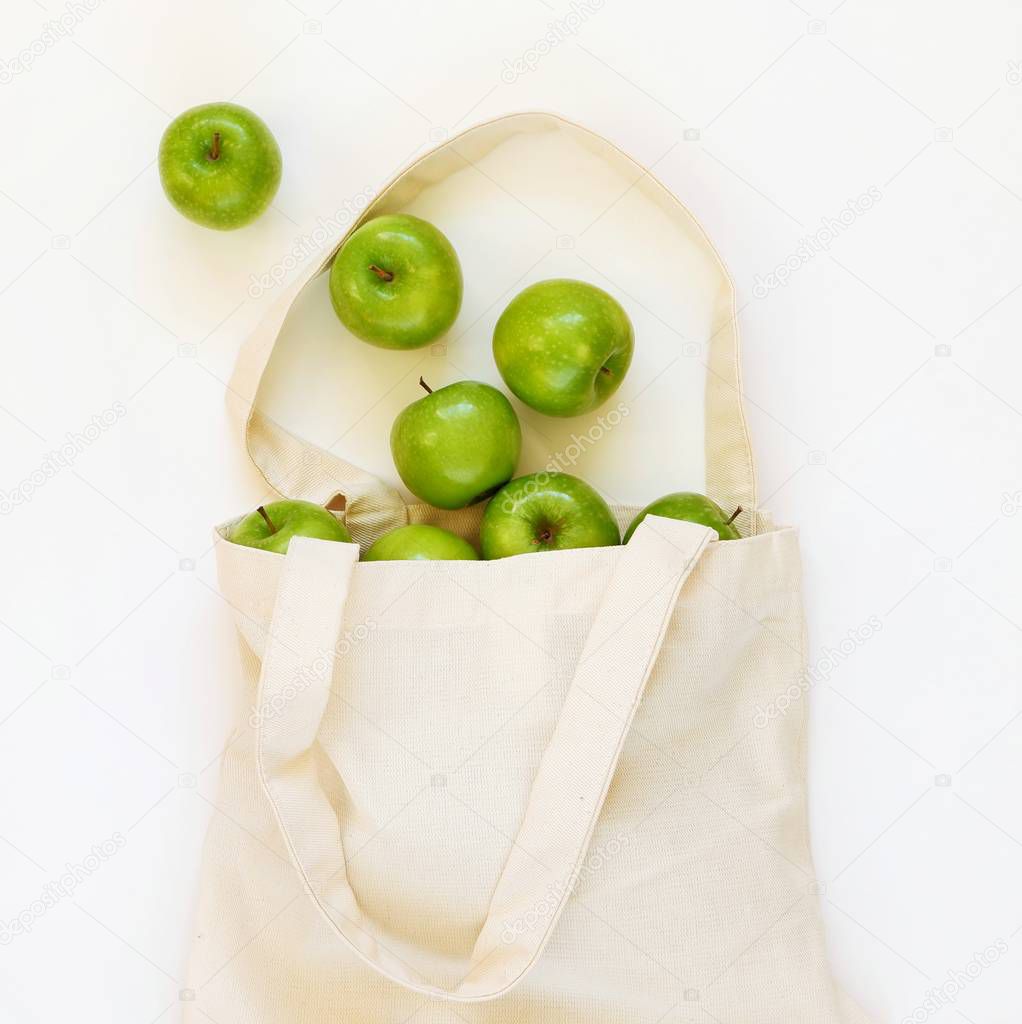 Reusable cotton textile bag with green apples on a white background. The concept of zero waste, green shopping. Square, top view with copy space for text.