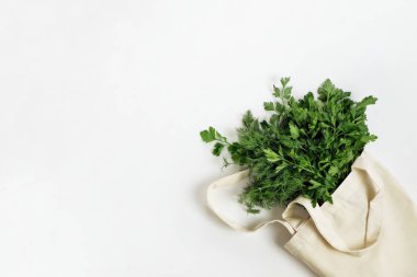 Bir demet taze organik maydanoz ve beyaz bir arka planda tekrar kullanılabilir pamuk torbası. Sağlıklı yiyecekler, organik ürünler, çevre dostu yaşam tarzı, sıfır atık kavramı. Üst görünüm, alanı kopyala.