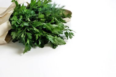 Bir demet taze organik maydanoz ve beyaz bir arka planda tekrar kullanılabilir pamuk torbası. Sağlıklı yiyecekler, organik ürünler, çevre dostu yaşam tarzı, sıfır atık kavramı. Kapat, boşluğu veya metni kopyala.