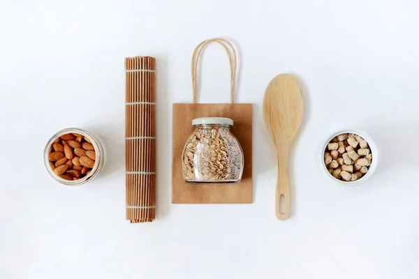 Sıfır atık kavramı, plastiksiz, yeniden kullanılabilir ambalaj. Üst kattaki kağıt torba, bambu hasırı, yulaf ezmeli cam kavanoz, granola, badem. Düz yatıyordu.