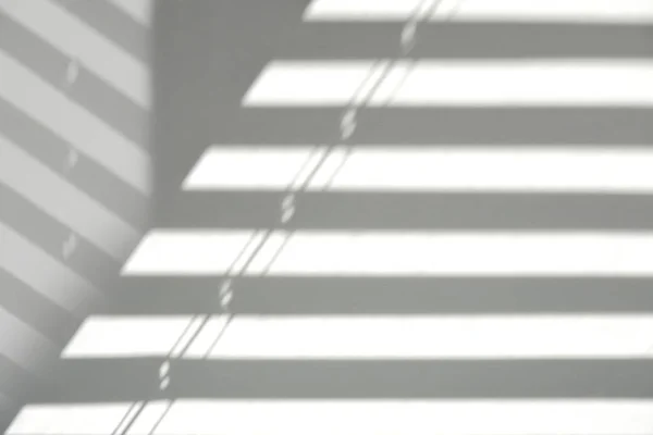 Light and shadows on a light wall through the window blinds. Diagonal parallel lines, abstract half frame composition. Copy space for text.