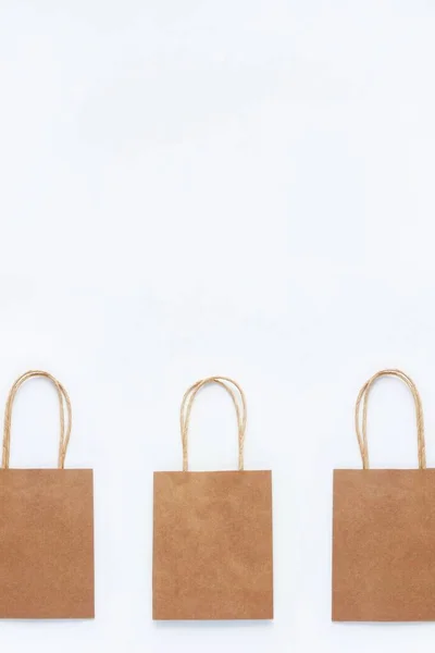 Brown craft bags for shopping on a white background in a row. The concept of zero waste, reasonable consumption, recycling, discounts. Vertical, top view, flat lay. Copy space.