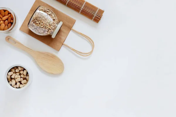 Sıfır atık kavramı, plastiksiz, yeniden kullanılabilir ambalaj. Üst manzara kağıt torbası, bambu hasırı, cam yulaf ezmesi kavanozu, hindistan cevizi, granola, badem. Düz yat, boşluğu kopyala.