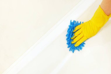 Mavi paspaslı sarı lastik eldivenli bir kadın eli beyaz bir küvetin yüzeyini yıkar ve parlatır. Bahar, düzenli bahar temizliği. Banyo Temizleme Konsepti. Metin için alanı kopyala.