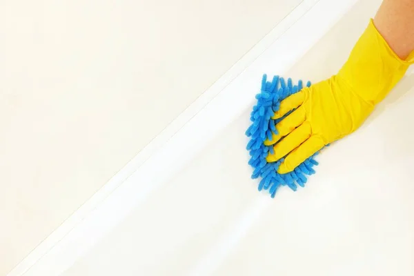 A female hand in a yellow rubber glove with a blue mop cloth washes and polishes the surface of a white bathtub. Spring, regular spring cleaning. Bathroom Cleaning Concept. Copy space for text.