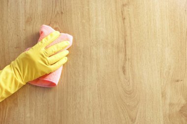 A man's hand in a yellow rubber glove oil polishes the wooden surface of the table, the floor with a pink rag. Cleaning company, spring cleaning at home.Concept finishing polishing furniture.Top view