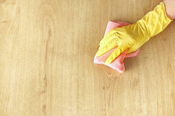 Sarı lastik eldivenli kadın eli, ahşap parke zemini pembe bir mikrofiber bezle yıkıyor. Üst görünüm, metin için boşluk kopyala.