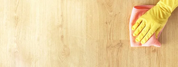 Sarı lastik eldivenli bir kadın, ahşap bir parke zemini pembe bir mikrofiber bezle yıkıyor. Temizlik hizmeti kavramı. Metin için kopyalama alanı olan üst görünüm pankartı.