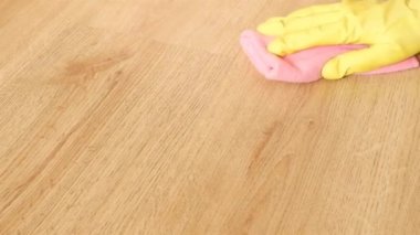 Sarı lastik eldivenli kadın eli, yakın plan, ahşap parke zemini pembe bir mikrofiber bezle yıkıyor. Ev temizliği kavramı.