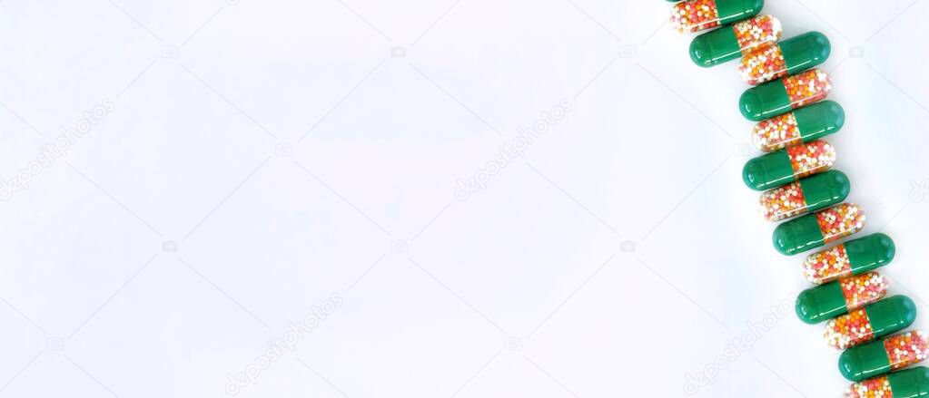 Medical capsules with colored granules in a row diagonally on a white background. The concept of health, medication, traditional treatment. Banner, flat lay, top view with copy space for text.