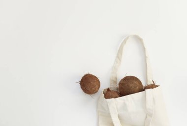 Beyaz arka planda, tekrar kullanılabilir pamuklu bir çantada hindistan cevizi. Sıfır atık kavramı, plastik serbest yaşam tarzı, organik gıda. Üst görünüm, düz görünüm, metin için alanı kopyala.