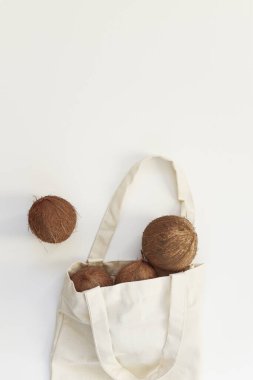 Beyaz arka planda, tekrar kullanılabilir pamuklu bir çantada hindistan cevizi. Sıfır atık kavramı, plastik serbest yaşam tarzı, organik gıda. Dikey, üst görünüm, düz görünüm, metin için boşluğu kopyala.