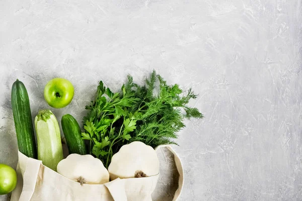 Çeşitli taze sebzeler ve meyveler, yeniden kullanılabilir bir alışveriş poşetinde çimento gri bir masa üstünde yeşillik, yemek blogu. Sıfır atık alışveriş kavramı. Kopyalama alanı olan üst görünüm.