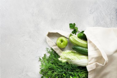 Çeşitli taze sebzeler ve meyveler, yeniden kullanılabilir bir alışveriş poşetinde çimento gri bir masa üstünde yeşillik, yemek blogu. Sıfır atık alışveriş kavramı. Kopyalama alanı olan üst görünüm.