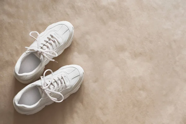 A pair of light-colored sneakers on craft wrapping paper. Minimalistic shoe background, fashion blog, women's sports shoes, stylish footwear. Top view, flat lay, copy space.