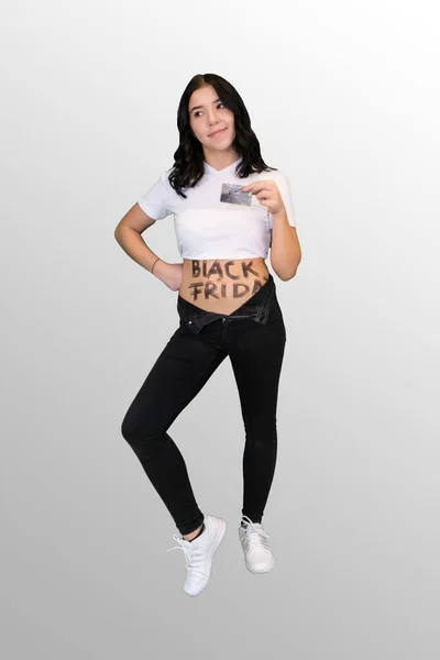 Chica joven tiene Viernes Negro escrito en su estómago y la celebración de una tarjeta de crédito en su mano —  Fotos de Stock
