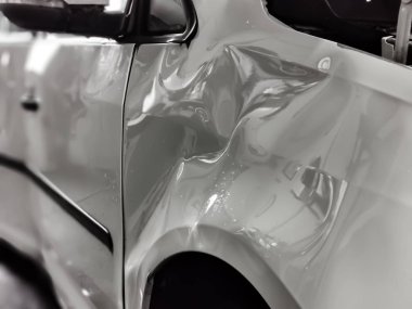 A small dent in the fender of a white metallic European car clipart