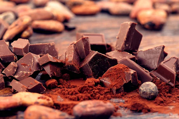 Broken dark chocolate, cocoa powder and coffee beans on a wooden table