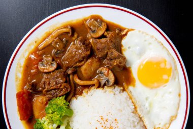 Siyah ahşap zemin üzerine köri pilavı (Onsen tamago, Patates, enoki mantarı, soğan, brokoli, Japon tarzı)