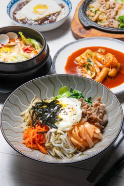 Bibimbap is served as a bowl of warm white rice topped with vegetables or kimchi and chili pepper paste and egg , sliced meat clipart