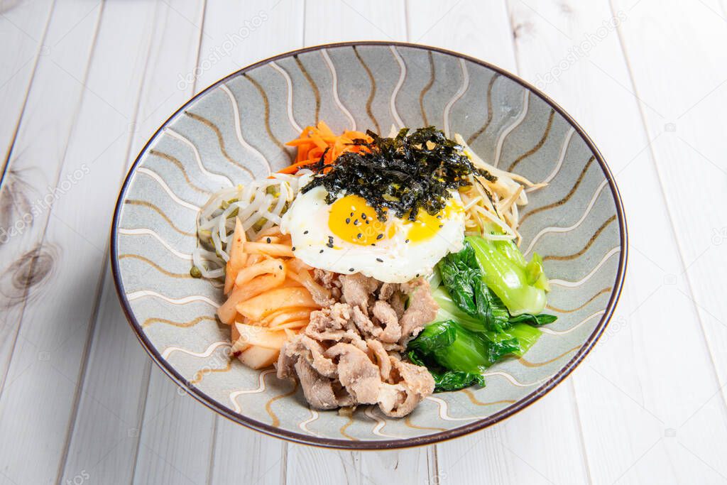 Bibimbap is served as a bowl of warm white rice topped with vegetables or kimchi and chili pepper paste and egg and sliced meat