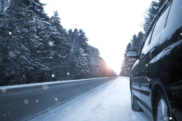 Kozalaklı ormanların arasında kış yolu, siyah araba, kar yağıyor.
