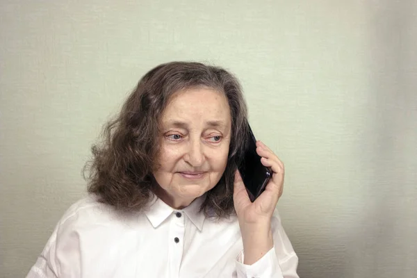 O femeie frumoasă în vârstă de aproximativ 65 de ani este fericită, zâmbind, vorbind pe un telefon mobil — Fotografie, imagine de stoc