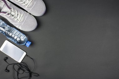Düz spor aletleri seti. Ayakkabı (spor ayakkabısı), plastik su şişesi, akıllı telefon, gri arka planda kulaklık. Aktif, sağlıklı bir yaşam tarzı. Metin için yer