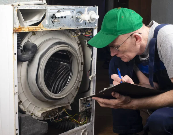 Çamaşır makinelerinin tamiri, büyük ev aletlerinin tamiri. Usta parçalanmış çamaşır makinesini ve arızaları inceliyor.