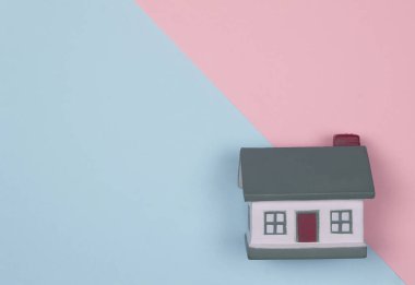 Pembe ve mavi arkaplanlı minyatür bir ev. Konsept ipotek, alım, satış, kiralık mülk. Mutluluk evdedir. Metin için yer
