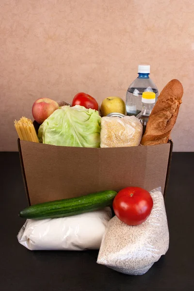 Box with products for delivery. Bottle water, vegetable oil, cereals, baguette, canned food, vegetables, sugar, rice. Copyspace. Vertical photo