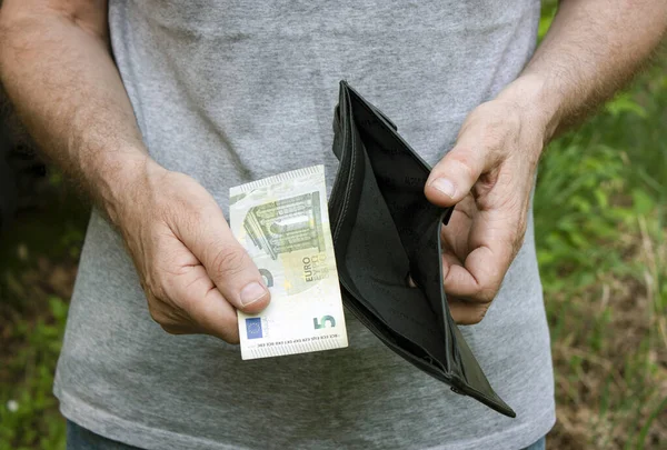 Bir adam ellerini tutuyor ve boş bir çanta ve beş avroluk banknot gösteriyor. Ekonomik ve finansal kriz, yoksulluk, işsizlik kavramı