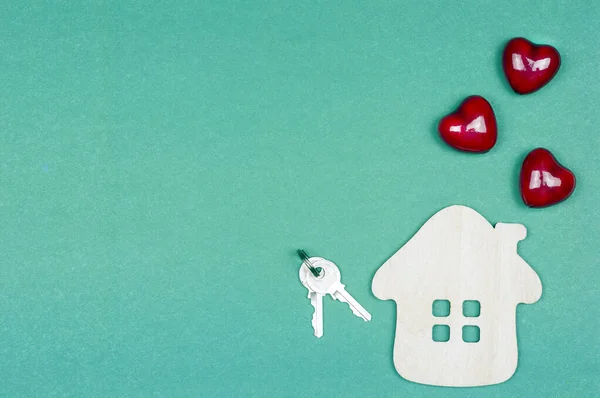 Küçük ahşap bir ev, kalpler borudan uçuyor, anahtarlar yeşil arka planda. Satın alma, satış, emlak kiralama ve ipotek konsepti. Ev inşaatı